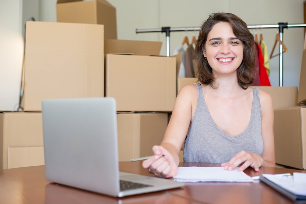 Happy woman working on a laptop surrounded by cardboard boxes. Ideal for business and online store concepts.